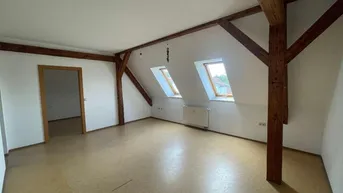 Heller Dachbodenraum mit sichtbaren Holzbalken, schrägen Decken und zwei Dachfenstern.