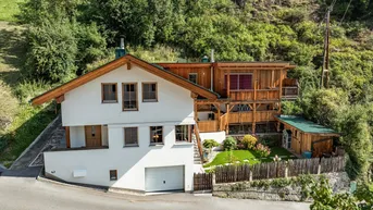 Charmantes Haus im alpinen Stil mit weißer Fassade, Holzverkleidung und integrierter Garage.