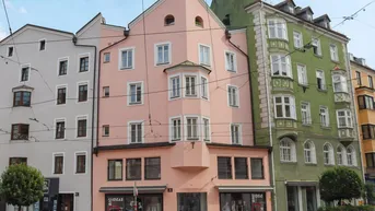 Historisches Gebäude mit markanter rosa Fassade und Geschäften im Erdgeschoss an einer belebten Straße.
