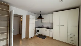 Helle Küchenzeile mit integrierten Schränken und Holzboden in einem offenen Wohnbereich.