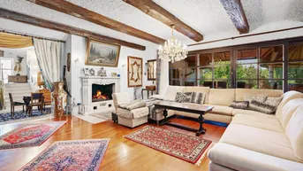 Elegantes Wohnzimmer mit Kamin, großem Sofa, Holzbalkendecke und Blick in den Garten.