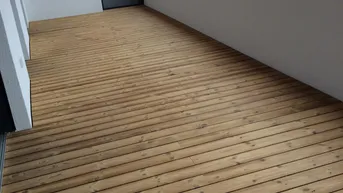 Geräumiger Balkon mit Holzboden und Blick auf die umliegenden Dächer, ideal für entspannte Stunden im Freien.