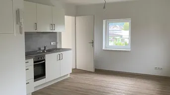 Heller offener Wohnbereich mit integrierter Küche und neuem Laminatboden.