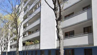 Mehrfamilienhaus mit mehreren Balkonen, umgeben von Bäumen und geparkten Autos auf der Straße.