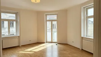 Heller Wohnraum mit Parkettboden, hohen Fenstern und Zugang zu einem französischen Balkon.