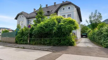 Historisches Gebäude mit gepflegter Fassade und üppiger Bepflanzung an der Straße.