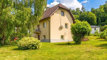 Gelbes Einfamilienhaus mit braunem Dach und grüner Umgebung unter blauem Himmel.