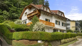 Traditionelles Haus mit gepflegtem Garten und Holzbalkonen an einem grünen Hang gelegen.