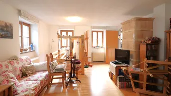 Helles Wohnzimmer mit traditionellem Kachelofen, Holzfußboden und großen Fenstern.
