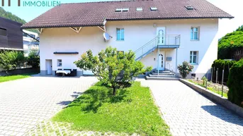 Vorderansicht des Hauses mit gepflasterter Einfahrt, kleinem Baum und Bergblick im Hintergrund.