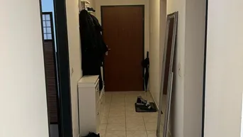 Langer Flur mit hellen Fliesen, weiß gestrichenen Wänden und einer Garderobe.
