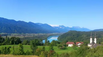 Panoramablick auf eine malerische Landschaft mit Bergen, einem Fluss und einem charmanten Dorf.