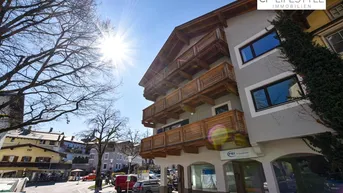 Fassade eines Mehrfamilienhauses mit Holzbalkonen und Blick auf die sonnige Straße.