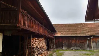 Alte Holzgebäude mit rustikalem Charme und einem großen Stapel Brennholz unter einem Vordach.