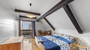 Gemütliches Schlafzimmer im Dachgeschoss mit sichtbaren Holzbalken, Holzboden und direktem Zugang zu einem Balkon.