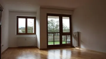 Helles Zimmer mit Holzboden, großen Fenstern und Blick ins Grüne.