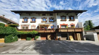 Traditionelles Mehrfamilienhaus mit weißer Fassade, Holzbalkonen und Garagen im Erdgeschoss.