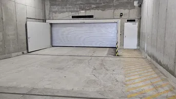 Geräumige Tiefgarage mit Betonwänden, Rolltor und ausreichend Platz für Fahrzeuge.