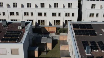 Luftaufnahme einer modernen Wohnanlage mit Reihenhäusern und Photovoltaikanlagen auf den Dächern.