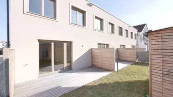 Moderne Reihenhausfassade mit Holzterrasse, kleinem Gartenbereich und Gartenhaus.