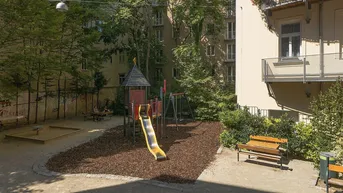 Gemeinschaftlicher Innenhof mit Spielplatz, Sandkasten und Sitzbänken, umgeben von Bäumen.