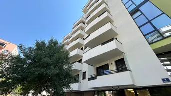Modernes Wohngebäude mit weißer Fassade, zahlreichen Balkonen und großen Glasflächen unter blauem Himmel.