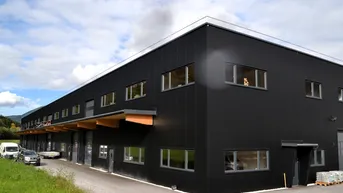Modernes Geschäftsgebäude mit schwarzer Fassade, großen Fenstern und Holzelementen unter einem Vordach.