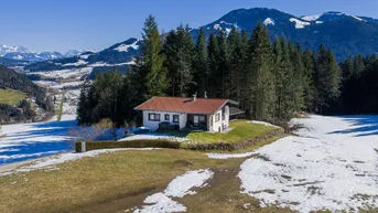 Weitläufige Luftaufnahme des Hauses in einer idyllischen Berglandschaft mit weiten Feldern und Wäldern.