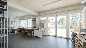 Geräumiger Werkstatt- oder Lagerraum mit großen Fenstern und direktem Zugang zum Außenbereich, ausgestattet mit Regalen und Arbeitsflächen.