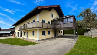 Gelbes Wohnhaus mit Balkon, Wintergarten und gepflegtem Vorgarten unter blauem Himmel.