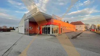 Modernes Geschäftsgebäude mit großzügigem Parkplatzbereich unter einem bewölkten Himmel und markanter Glasfront.