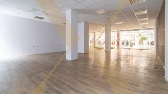 Geräumige, leere Gewerbefläche mit Säulen, abgehängter Decke und großen Schaufenstern zu einem Einkaufsbereich.