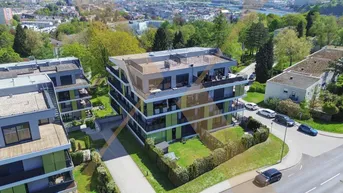 Moderne Wohngebäude mit Flachdächern und Balkonen, umgeben von viel Grün und Stadtblick.