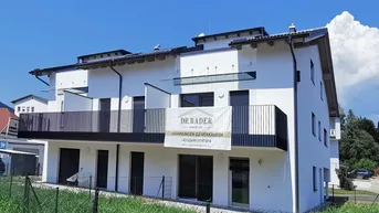 Weißes Mehrfamilienhaus mit modernen Balkonen und einem Verkaufsbanner unter blauem Himmel.