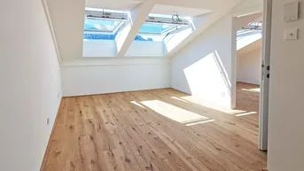Heller Raum im Dachgeschoss mit Holzboden, schrägen Wänden und mehreren Dachfenstern.