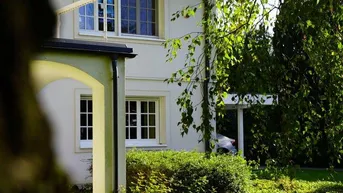 Teilansicht des Hauses mit gepflegtem Vorgarten und üppigem Grün an einem sonnigen Tag.