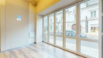 Heller Innenraum mit großen Fenstern zur Straße und Holzboden, ideal für ein Geschäft oder Büro.