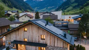 Abendansicht des Chalets mit Solaranlage auf dem Dach, Pool und beleuchteter Bergkulisse.
