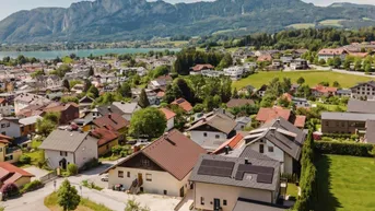 Luftaufnahme einer Wohnsiedlung mit See- und Bergblick, einige Häuser mit Solaranlagen.