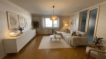 Helles und modern eingerichtetes Wohnzimmer mit beigem Ecksofa, Holzboden und großen Fenstern.