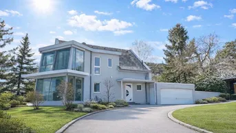 Modernes Einfamilienhaus mit großer Glasfassade, Auffahrt und integrierter Garage unter blauem Himmel.
