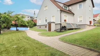 Seitenansicht des Hauses mit gepflastertem Weg, aufblasbarem Pool und Solarkollektoren.