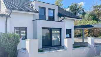 Moderne Hausfassade mit großen Fenstern, Balkon und Carport unter blauem Himmel.