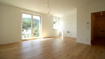 Helles Wohnzimmer mit Holzboden, großen Fenstern und Zugang zu einem kleinen Balkon mit grüner Aussicht.