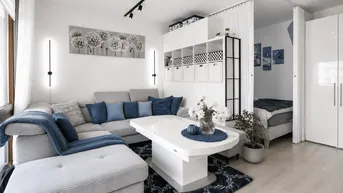 Helles Wohnzimmer mit modernem Sofa, Couchtisch und integriertem Schlafbereich, abgetrennt durch einen Vorhang.
