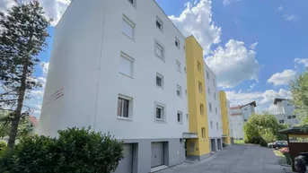Modernes Mehrfamilienhaus mit weißer und gelber Fassade sowie Garagen im Erdgeschoss.