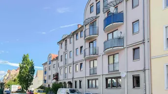 Mehrfamilienhaus mit mehreren Balkonen und Satellitenschüsseln an der Fassade, umgeben von parkenden Autos.