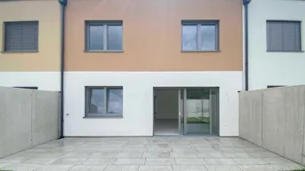 Rückseite eines Reihenhauses mit gepflasterter Terrasse und kleinem Rasenbereich.