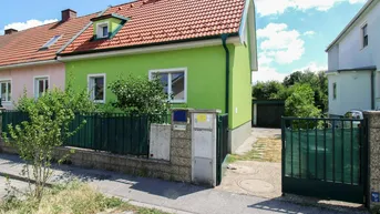 Grünes Einfamilienhaus mit rotem Ziegeldach, Vorgarten und Zufahrt zur Garage.