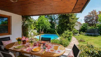 Überdachte Terrasse mit Esstisch und Blick auf den Garten mit privatem Pool und Trampolin.